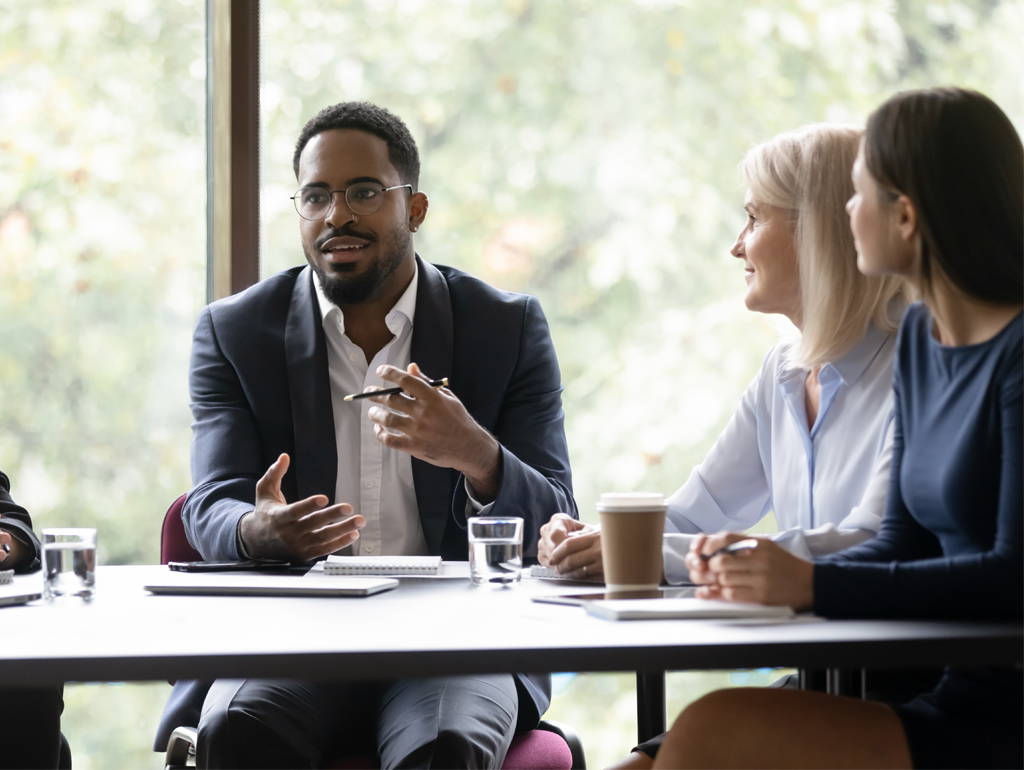 Man speaking at a table with two women paying attention to him